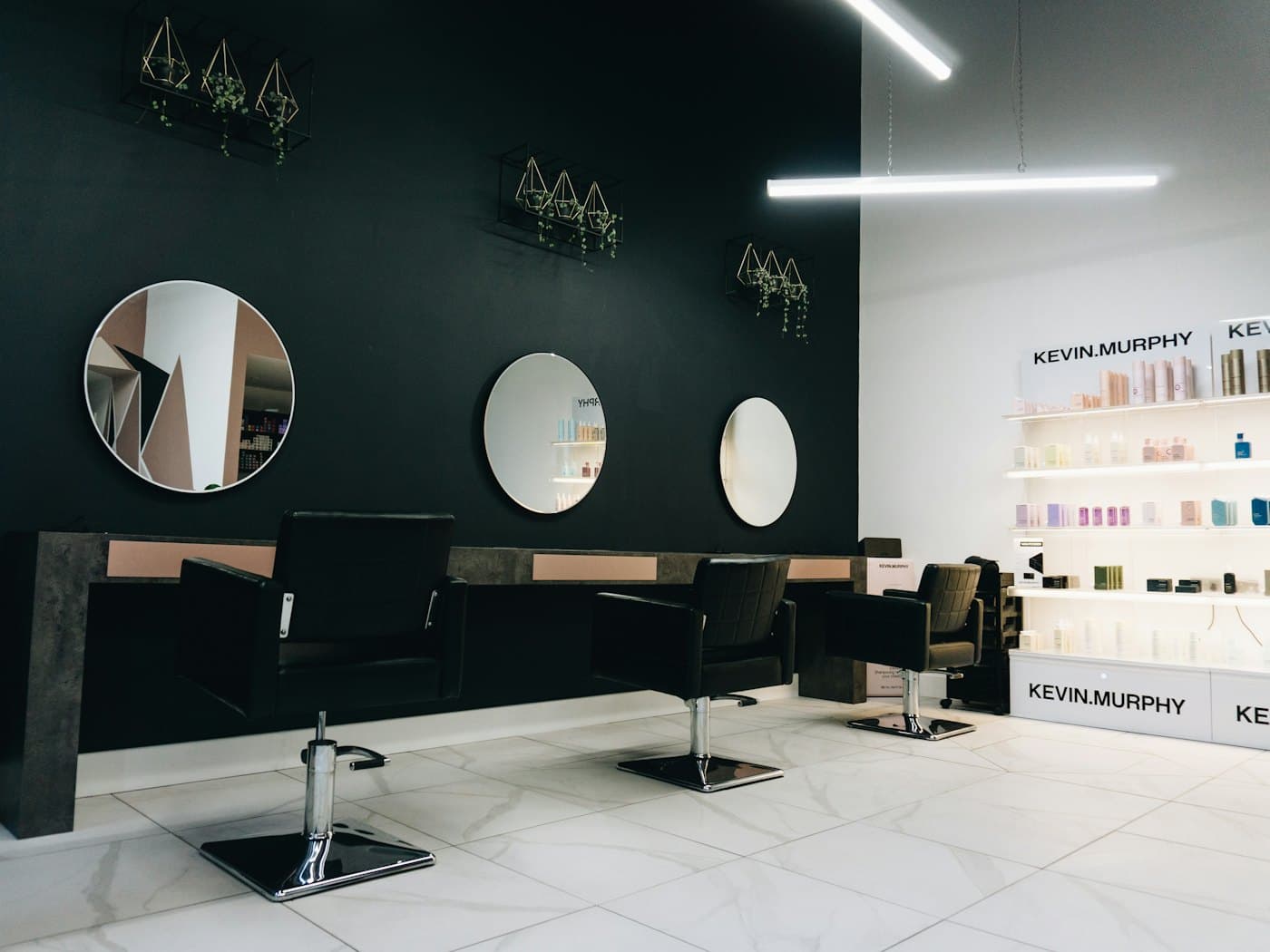 Un salon de coiffure vide, fauteuils noirs face aux miroirs ronds